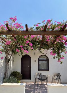 a white house with pink flowers growing over it's roof and patio furniture on the outside