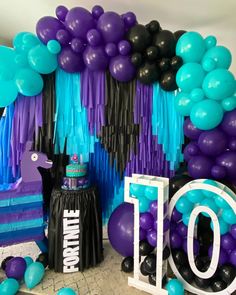 balloons and streamers decorate the backdrop for a 10th birthday party in purple, teal, and black