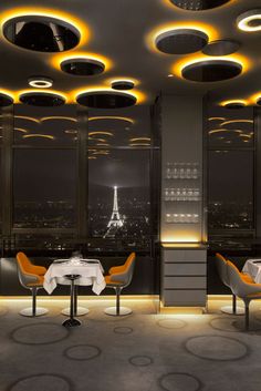 a dining room with tables and chairs in front of large windows overlooking the city at night