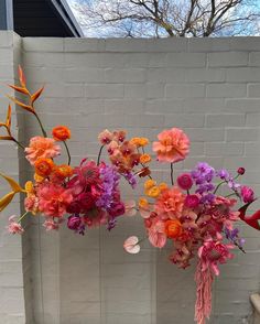 three vases filled with different colored flowers on top of a wooden table in front of a white brick wall