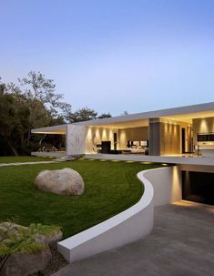 a modern house with grass and rocks in the front yard at dusk, as seen from across the driveway