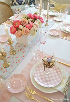 the table is set with pink and white plates, silverware, and flowers in vases