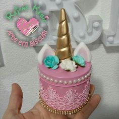 a hand holding a pink and gold cake with a unicorn horn on it's top