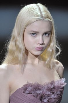 a model with blonde hair and blue eyes wearing a purple dress on the catwalk