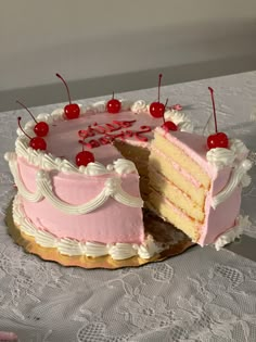 a pink cake with two slices cut out and cherries on the top is sitting on a lace tablecloth