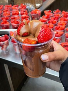 a person holding up a plastic cup with strawberries in it and chocolate on top