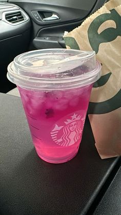 a pink drink sitting on top of a table next to a paper bag and a car steering wheel