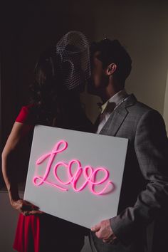 a man and woman holding a neon sign that says love