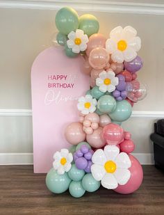 the balloon arch is decorated with flowers and balloons in pastel colors, along with a happy birthday sign