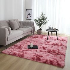 a living room with a couch, coffee table and pink rug on the floor in front of a window