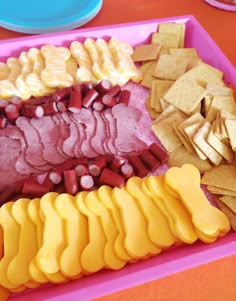 a tray filled with meat, cheese and crackers on top of a red table