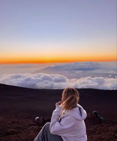 a woman sitting on top of a mountain looking at the clouds