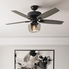 a ceiling fan with a light on top of it in a living room next to a painting