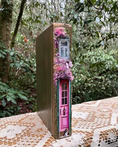 an open book with flowers on it sitting on a table in front of some trees