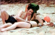 a man and woman laying on the beach in swimsuits next to an orange frisbee