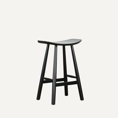 the stool is made from black wood and has a curved seat on one side, while the