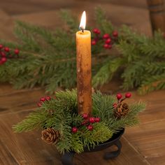 a candle that is sitting in a bowl with pine cones and berries on the table