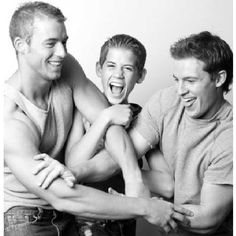 three young men laughing while sitting on a chair together with their arms around each other