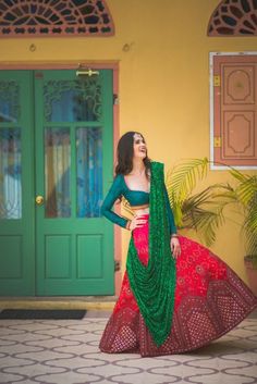 a woman standing in front of a green door wearing a red and green lehenga