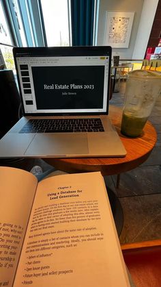 an open book sitting on top of a table next to a laptop computer and drink