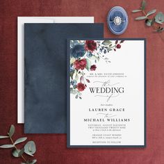 a wedding card with flowers on it next to a blue and white envelope, surrounded by greenery