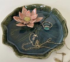 a green plate with a flower on it next to a chain bracelet and ring holder