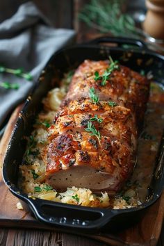 a pork roast with potatoes and herbs in a black pan on a wooden cutting board