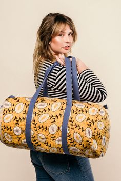 a woman holding a large yellow and blue duffel bag on her shoulder while standing in front of a white wall