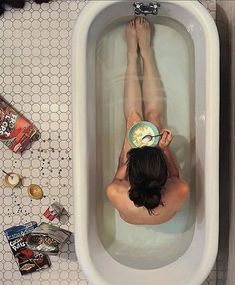 a woman laying down in a bathtub with food on the floor and around her