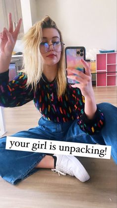 a woman sitting on the floor taking a selfie with her cell phone and wearing glasses