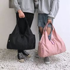 two people standing next to each other with bags in front of their faces and one holding a pink bag