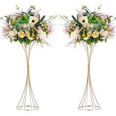 two tall metal vases with flowers and greenery on each one, side by side