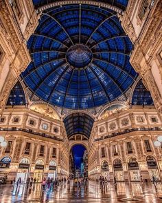 the inside of a large building with many windows and people walking around it at night