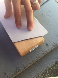 a person's hand on top of a piece of paper next to a wooden plank