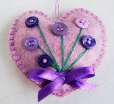 a heart shaped ornament with buttons and purple ribbon on the top, hanging from a string