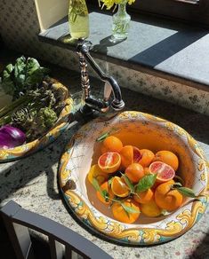 oranges and other fruits are in a bowl on the counter next to a vase with flowers