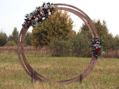 a wooden circle with flowers and greenery on it in the middle of a field