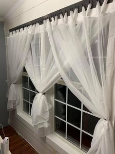 a window with white curtains and bow ties hanging from it's sides, in front of a wooden floor