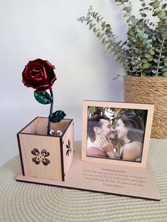 a wooden box with a rose in it next to a photo frame and a flower