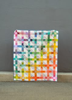 a multicolored quilt sitting on the ground next to a gray wall and cement floor