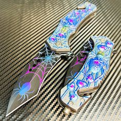 two colorful knives sitting on top of a black and white checkered table cloth with spider web designs