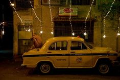 an old yellow taxi cab parked in front of a building with christmas lights strung across it