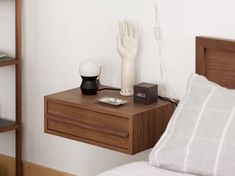 a bedside table with an alarm clock, lamp and hand statue on it next to a bed