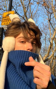 a man wearing a blue sweater and white mittens is covering his face while standing next to a street sign