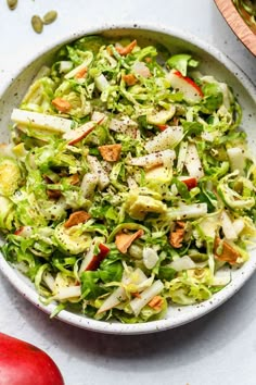 a white bowl filled with lettuce salad next to an apple and other vegetables