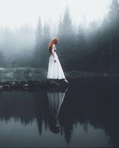 a woman in a white dress is standing on the edge of a body of water