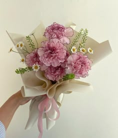 a bouquet of pink carnations and daisies is held by a woman's hand