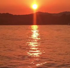 the sun is setting over the water with mountains in the background