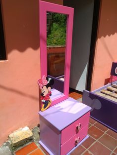 a pink and purple vanity with a mickey mouse mirror on it's stand next to a bed