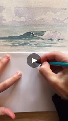 two hands are holding pencils and drawing an ocean scene